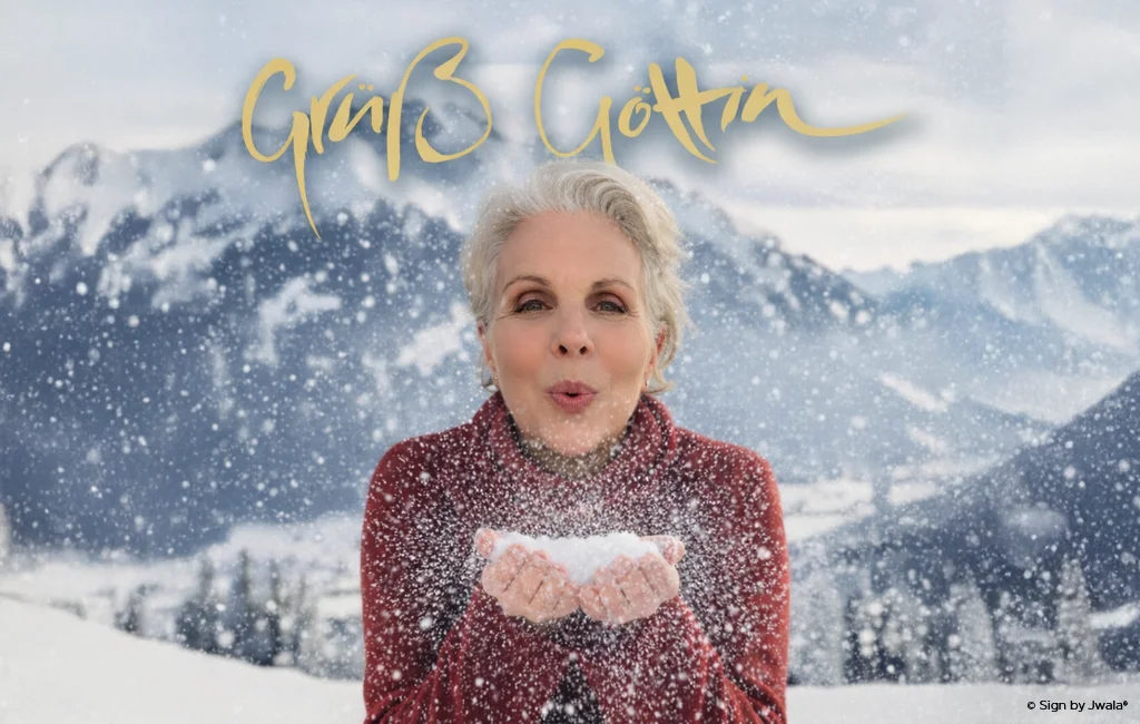 Jwala, die Inhaberin des SignShop Tirol, bläst Schnee in die Luft vor einer verschneiten Winterlandschaft