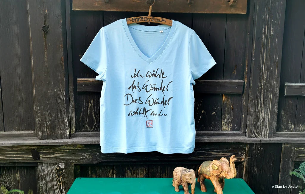 Blaues T-Shirt mit inspirierender Botschaft an einer Holzwand aus dem Onlineshop SignShop Tirol.