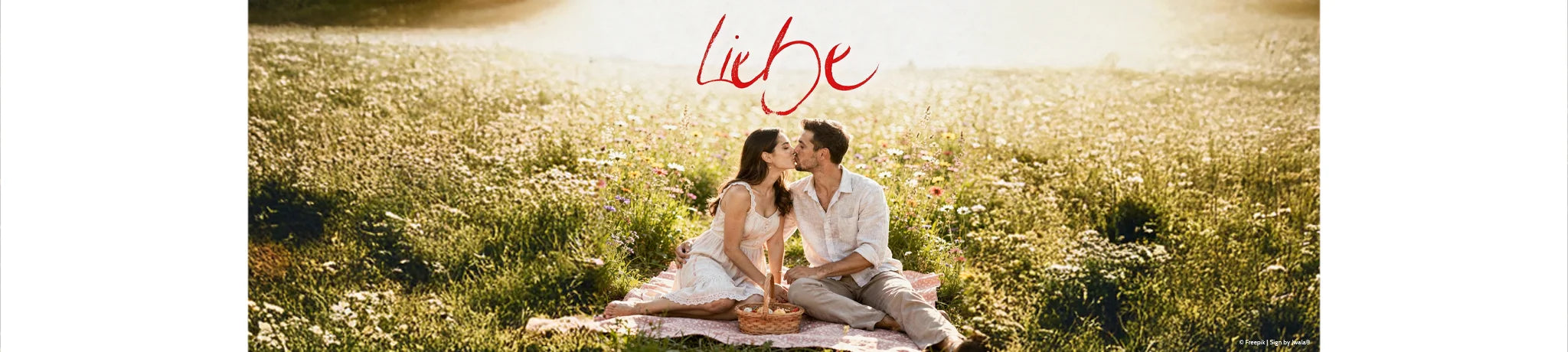 Pärchen auf einer Decke in der Wiese, das sich küsst; oben steht die Jwala-Botschaft „Liebe“ – aus dem Onlineshop SignShop Tirol.