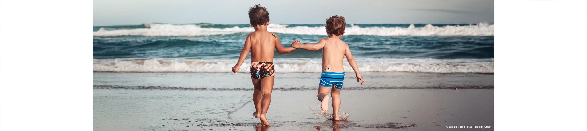 Zwei Kinder am Sandstrand am Wasser, beide tragen ein inspirierendes Hauttattoo aus dem SignShop Tirol, das sie dort gekauft haben.